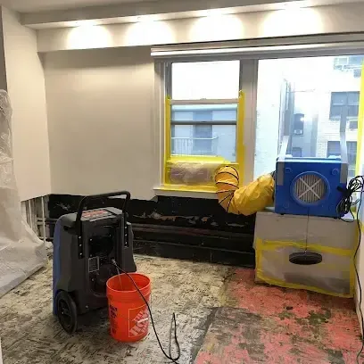 A dehumidifier and an air mover working in a room with the flooring removed
