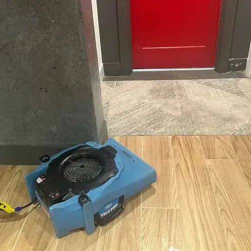 An air mover on a wood-look tile floor beside an open doorway during drying