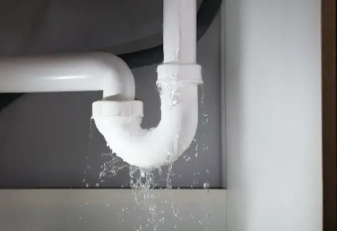 A leaking pipe dripping under a kitchen sink
