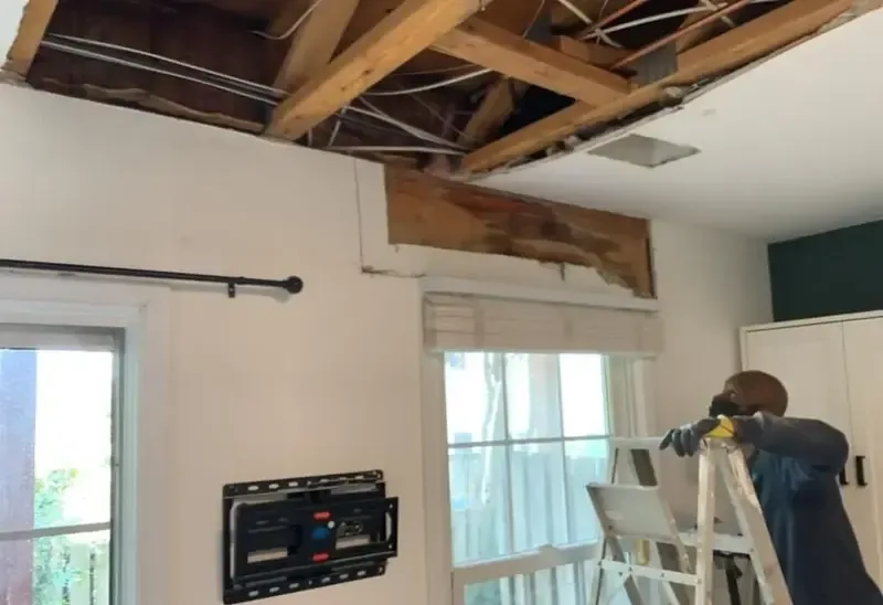 A worker on a ladder beneath a ceiling opened to the rafters after a roof leak