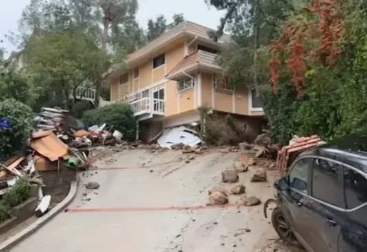 Mud and storm debris washed across a sloped street outside a two-story house